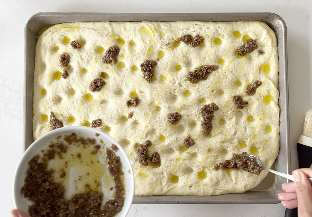 Spreading anchovy dressing over pissaladière dough // FoodNouveau.com